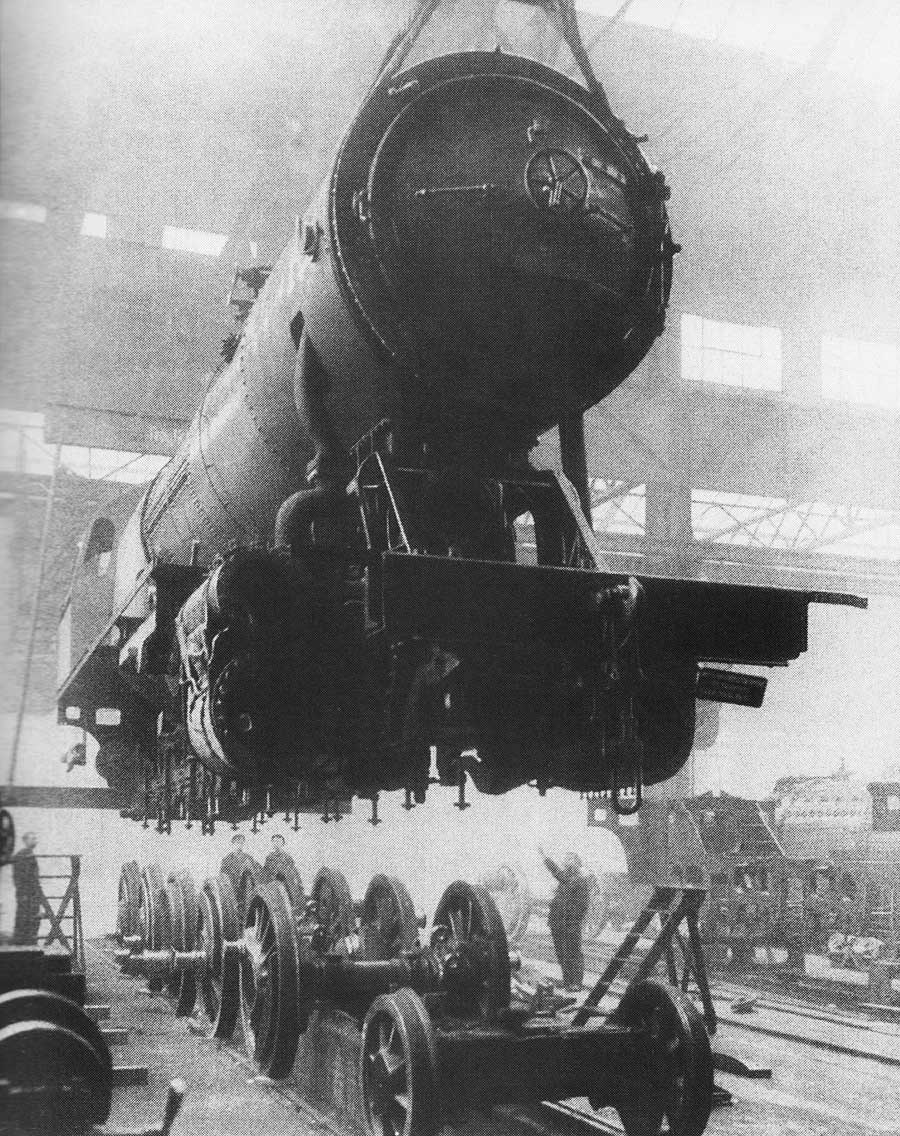 Historisches Foto: ein großer Tank aus Stahl schwebt mit Hilfe eines Krahns oder einer Seilwinde über den zu montierenen Schinenrädern.